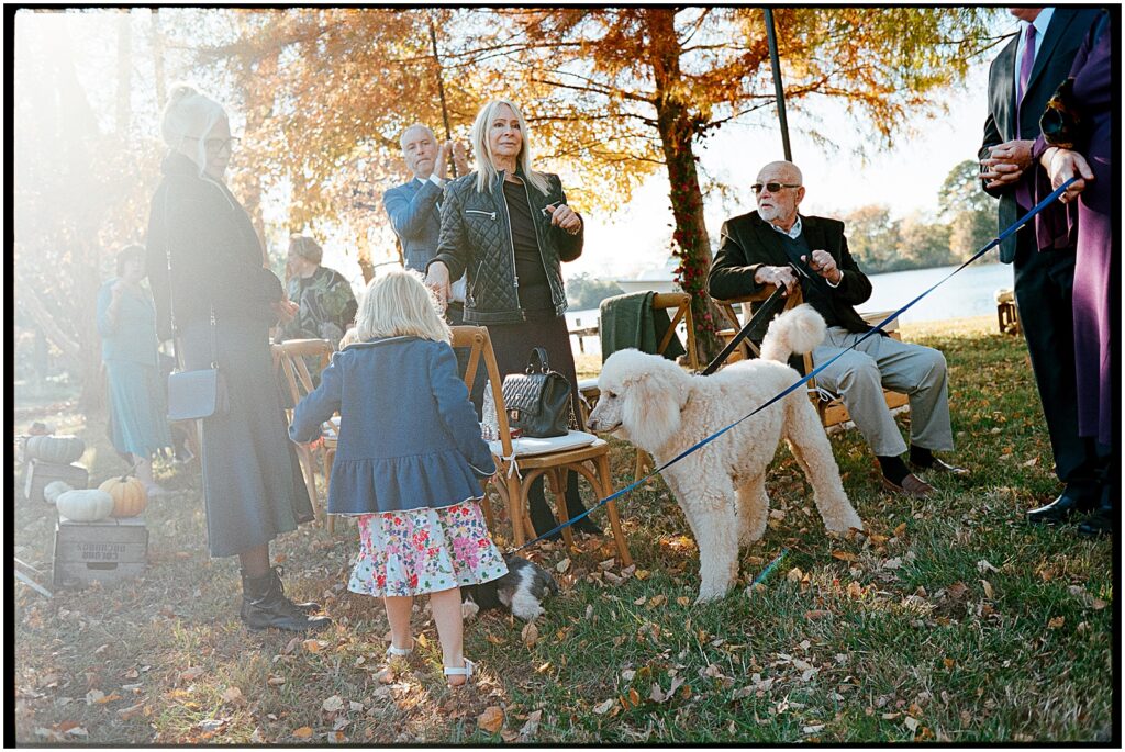 Wedding guests, including a child and dog, arrive for a lake house wedding ceremony.