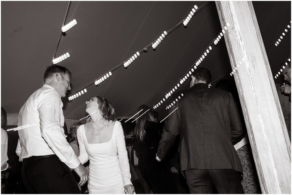 Lights blur behind a bride and groom in a wedding tent in a modern wedding photo.