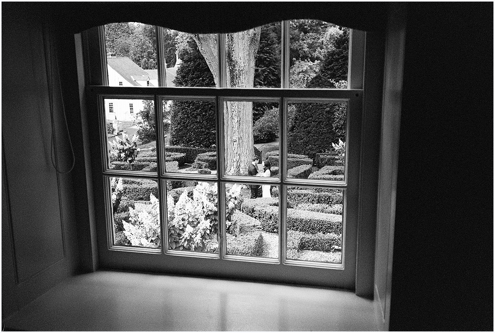 A Philadelphia photographer takes a wedding portrait through a window of a couple in a courtyard.