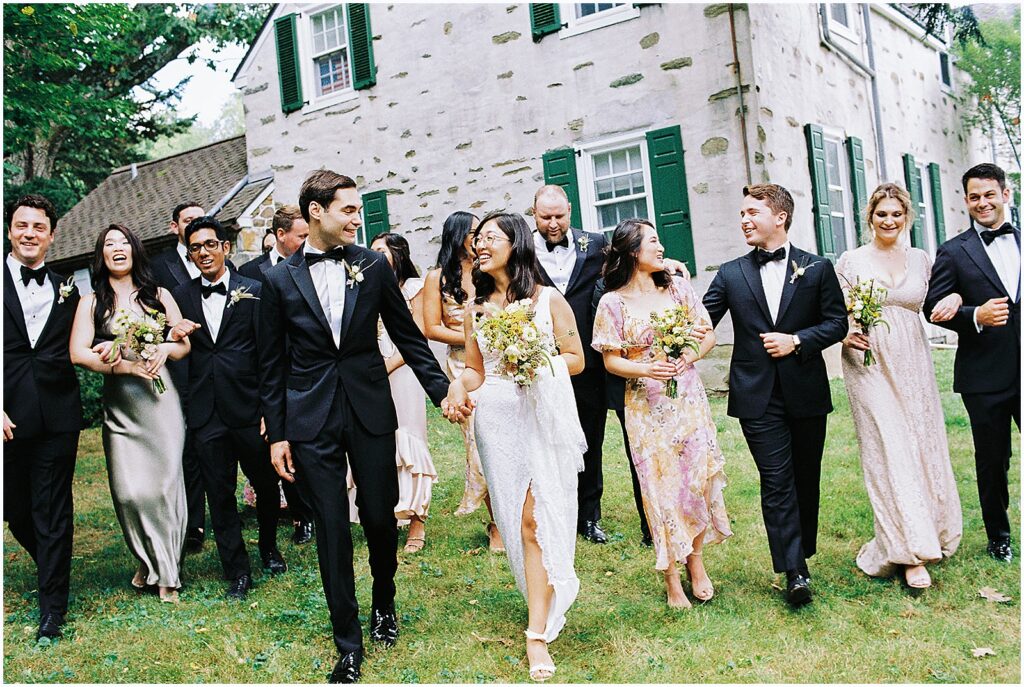 A bride and groom walk across a lawn with their wedding party for wedding party portraits in Philadelphia.