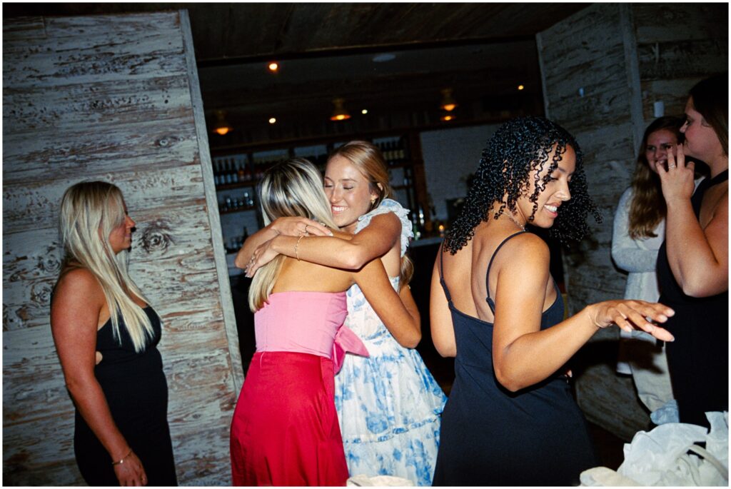 A bride hugs her bridesmaids at a rehearsal dinner.
