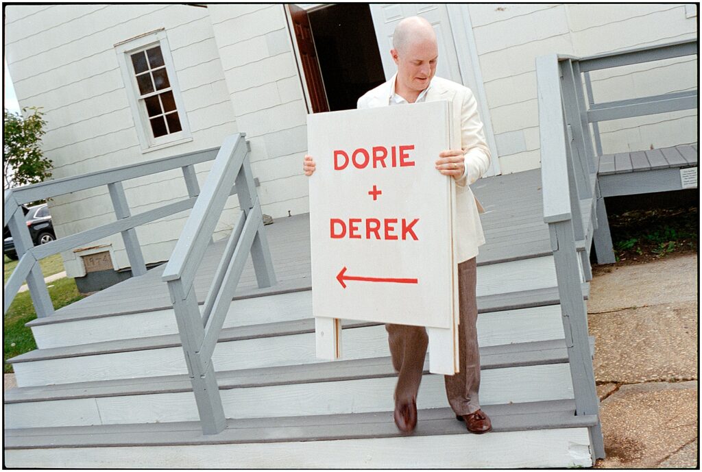 A groom carries a wedding sign down the steps at the Sandy Hook Chapel.