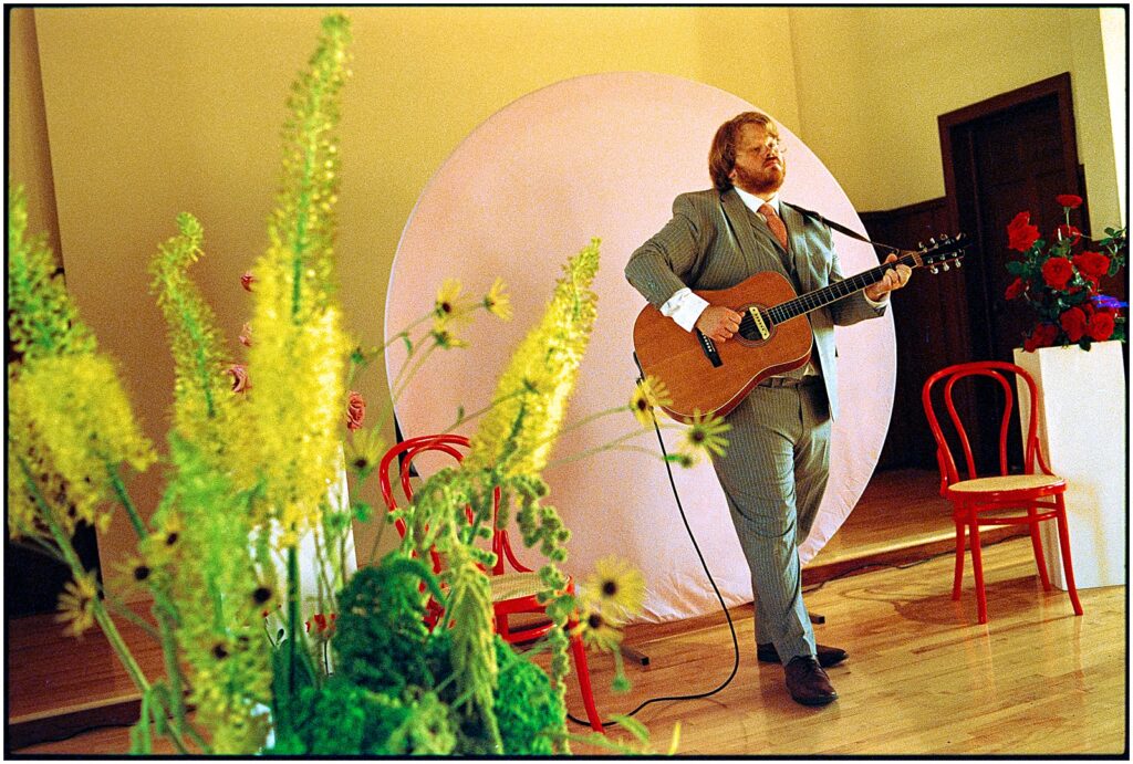 A guitar player stands in front of a pink wedding ceremony backdrop.