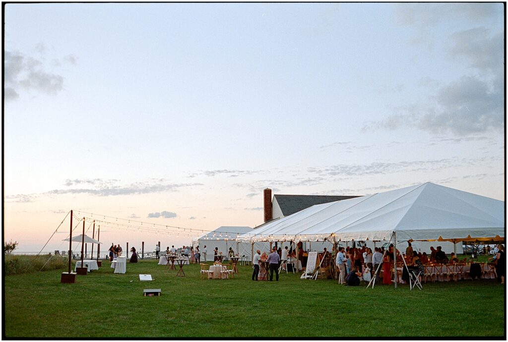 Wedding guests gather inside a white tent as the sun sets behind Sandy Hook Chapel.