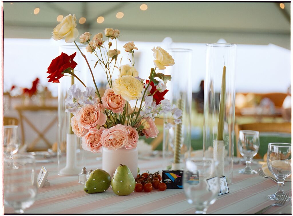 A creative wedding bouquet sits on a reception table beside fruit and candles.