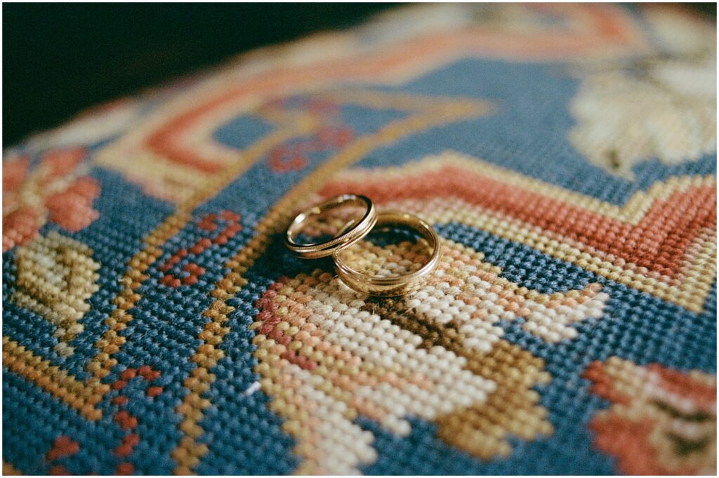 Two gold wedding rings sit on a brightly colored rug.