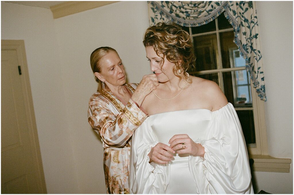 A bride's mother helps her fasten her modern wedding dress.