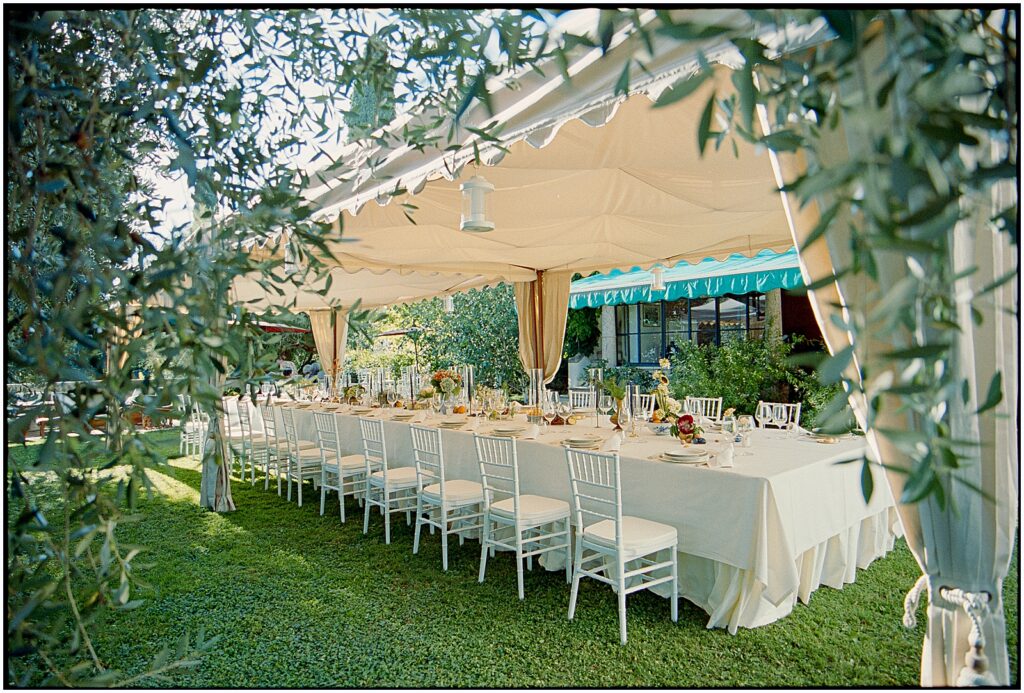 A long reception table sits under a tent at an Italian wedding venue.