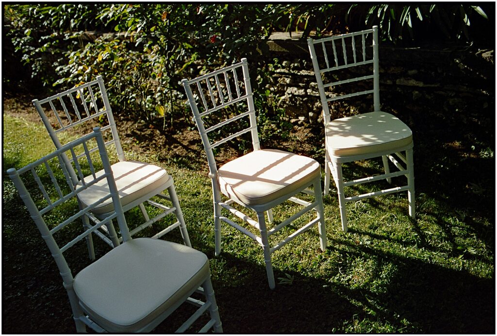 Sunlight shines on white chairs on a lawn.