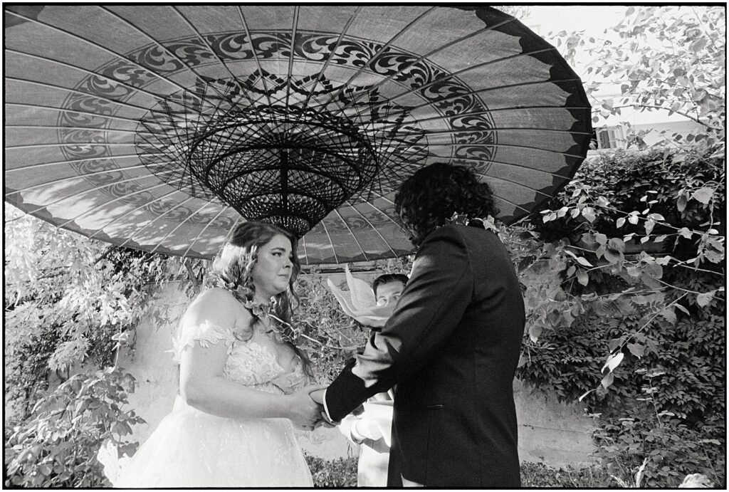 A bride and groom stand under an oversized parasol for their wedding in Italy.
