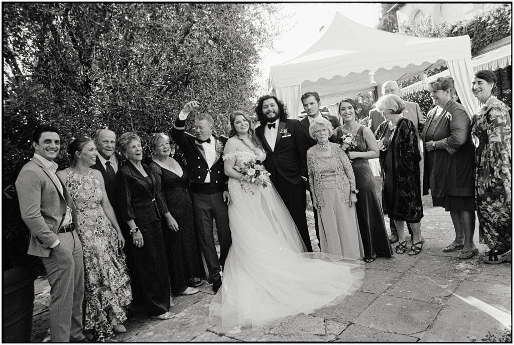 Family members stand on either side of a bride and groom for a group wedding photo.