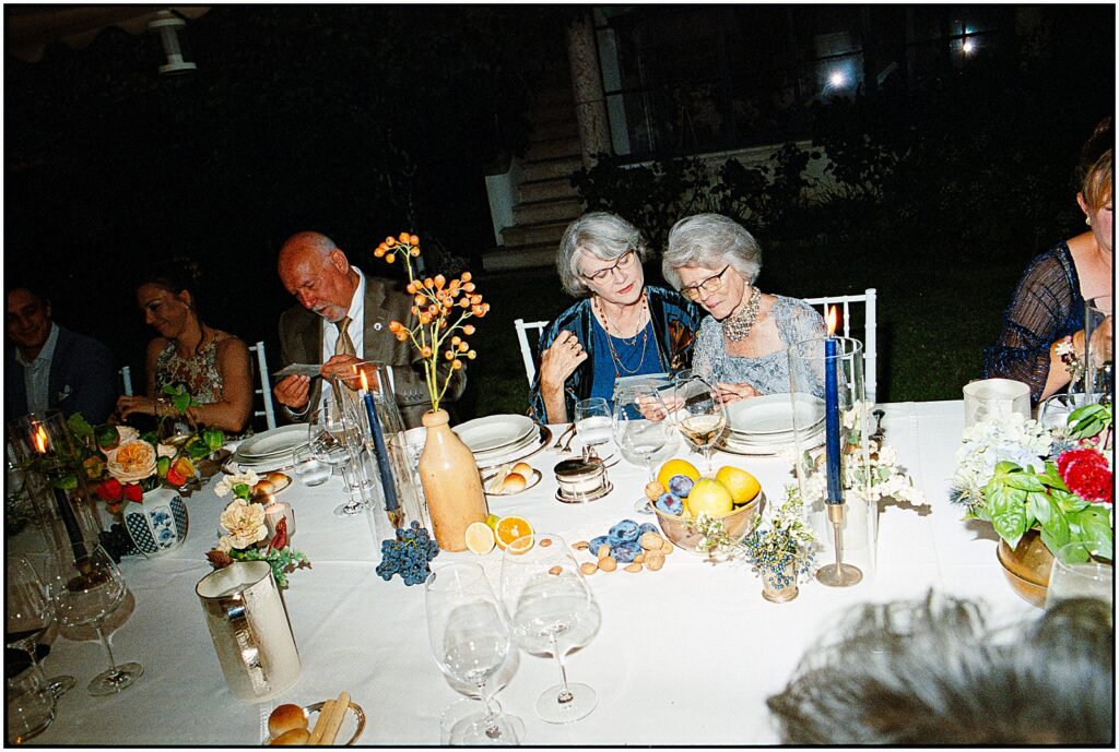 Two women sit talking at a candlelit dinner table at a destination wedding in Italy.