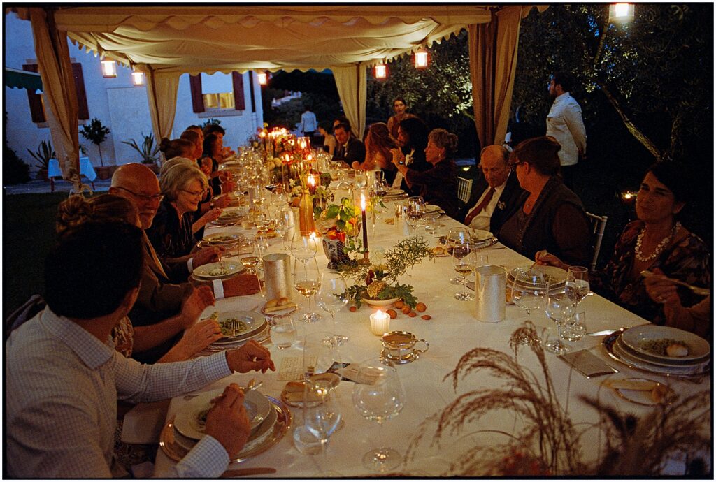 Wedding guests gather at a long candle-lit table under a tent in Italy.