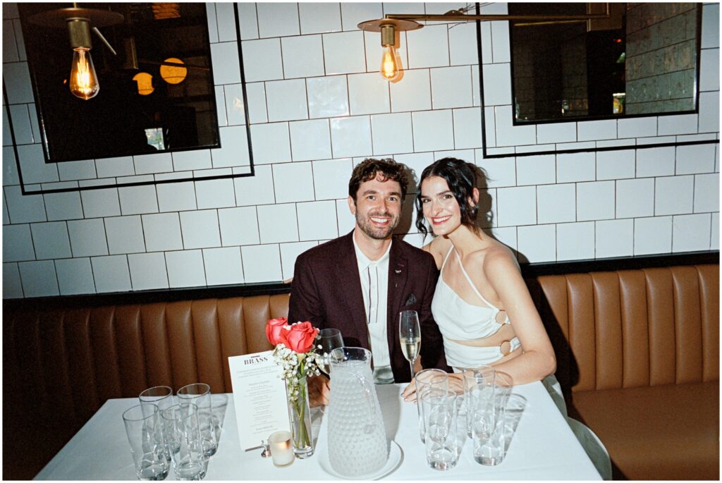The couple sits together, beaming with happiness, at their engagement party at American Brass in Long Island City, NY